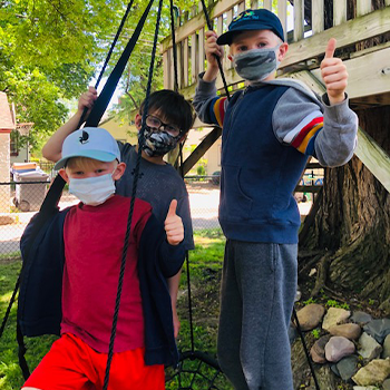 Three boys play outside with camouflage patterned face masks
