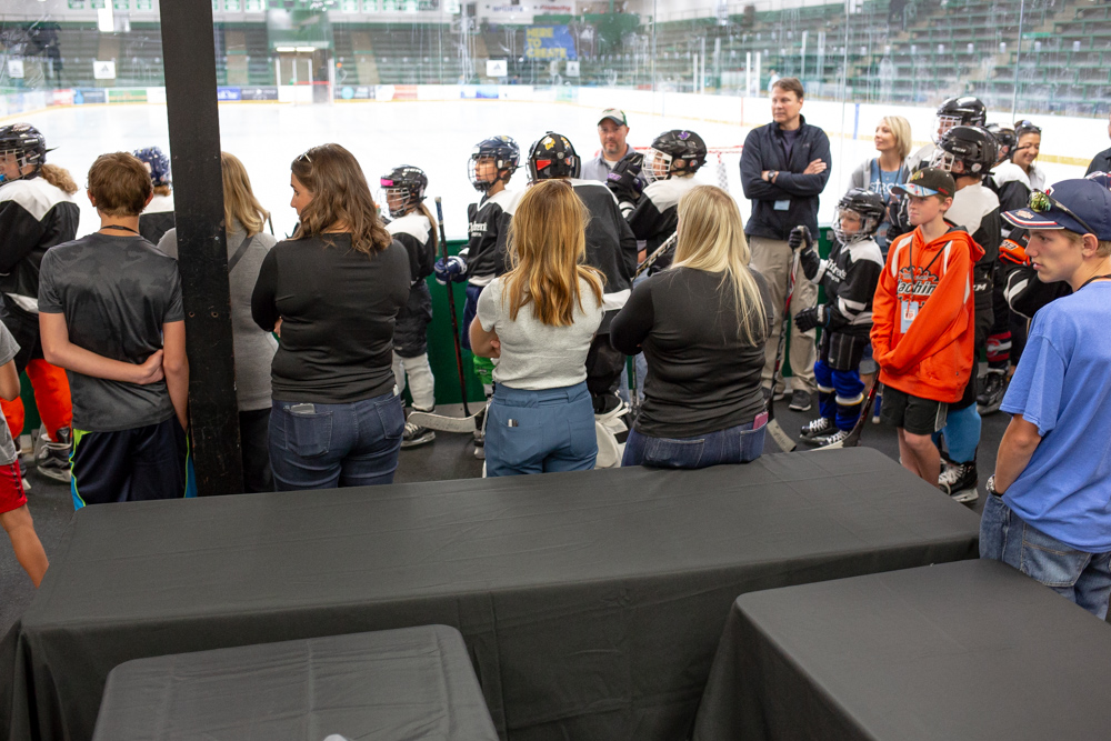 The backs of a line of stands who are looking in to a hockey arena