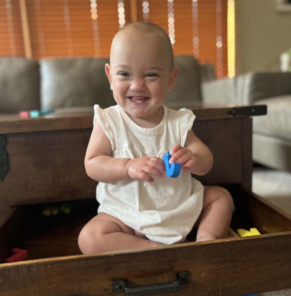 Baby Myah plays with foam letters and smiles at the camera.
