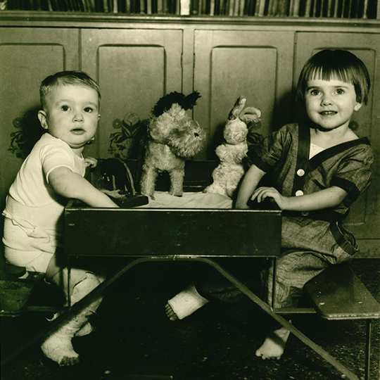 Two young children sit at a small table filled with toys.