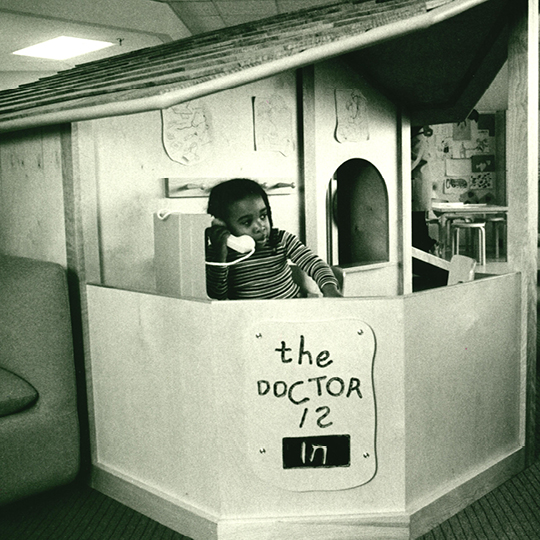 a small child is playing in a playhouse talking on a phone. The front of the playhouse has a sign that reads, "the doctor is in"