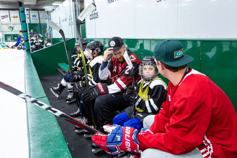 Two hockey players in red jerseys talking to a young boy in hockey gear
