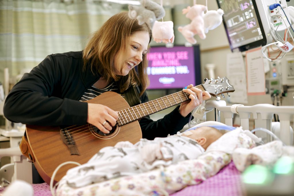 Music therapist plays music for a baby in the NICU
