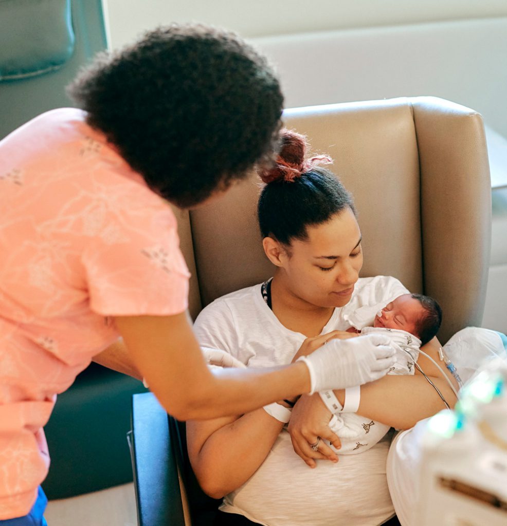 Mom holding baby and nurse leaning over to care for baby