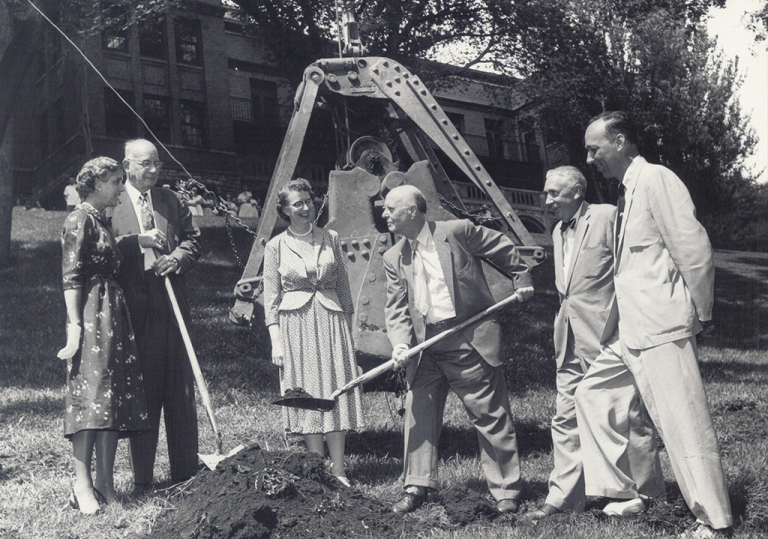 Hospital founder Dr. Walter Ramsey shovels dirt while administrator Eleanor Sackett and others look on.