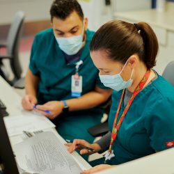 two people wearing scrubs and masks review documents at a desk
