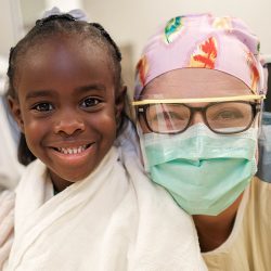 a patient smiles with their doctor who is wearing a mask and protective eye coverings