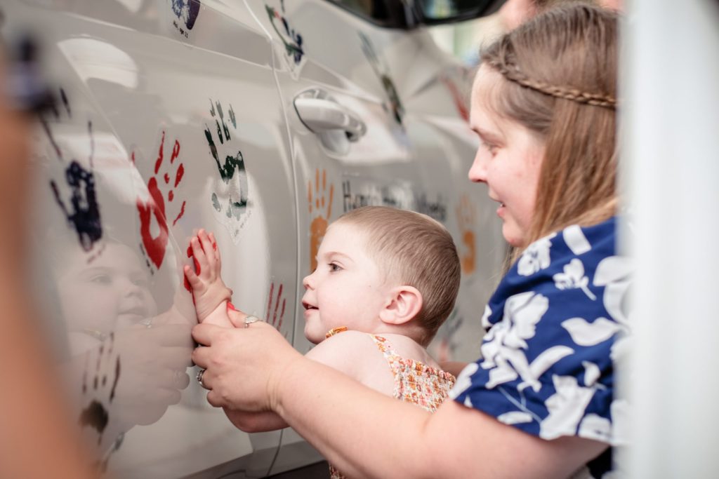 Avery, leukemia patient, placing her painted handprint on vehicle with help from her mom, Allison.