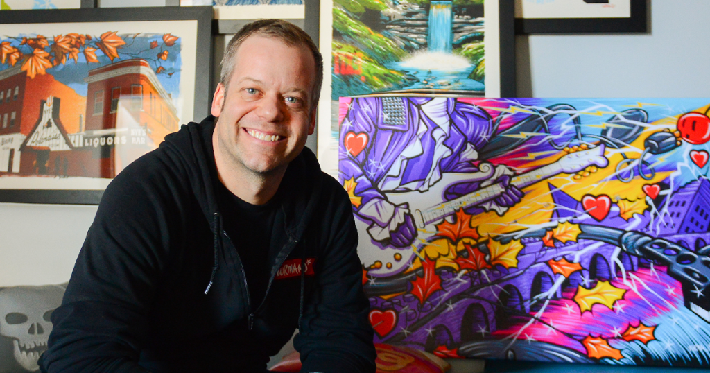 Adam Turman smiling with his artwork behind him