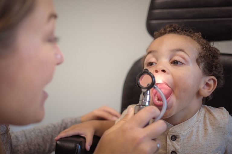 Little boy with his mouth open getting his tonsils checked by a doctor