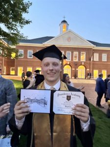 Alec Santelman holds his high school diploma while wearing a graduation cap and gown at his Providence Academy graduation.