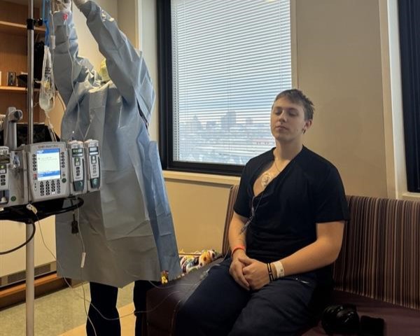 Alec Santelman sits in a clinic chair as medication is administered through infusion equipment during cancer treatment.