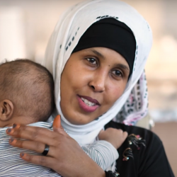 Amina, who wears a hijab, hugs her son while smiling at the camera