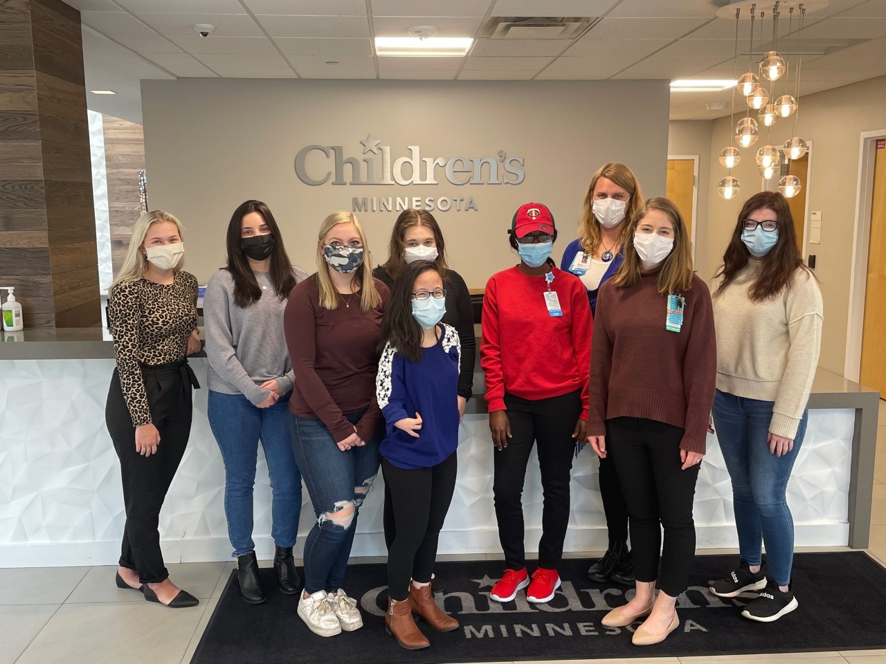 Nine CSAs stand in front of a counter and a Children's Minnesota sign. They're all wearing masks.