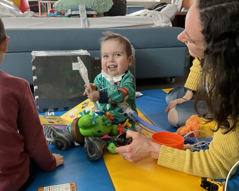 Archer Boman smiling and opening a gift in his hospital room at Children's Minnesota.