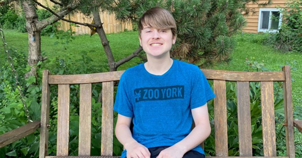 Ben Menier sitting outside on a bench in a blue shirt