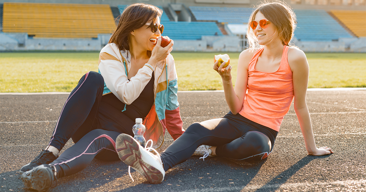Mother and teenage daughter eating apples after going for a walk
