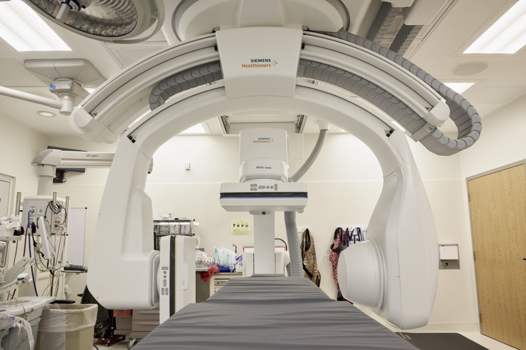 Photo zooms in on an operating bed with a large circular imaging tool surrounding it that can rotate around the patient.