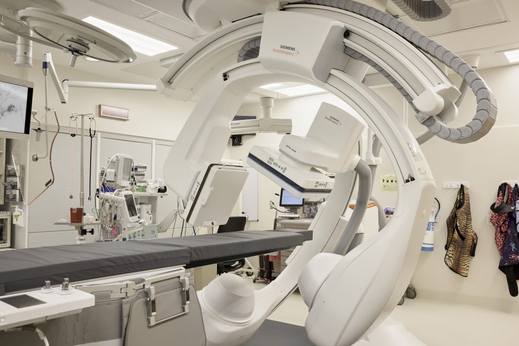 Operating room is shown with a bed that has a large imaging device around it that is mid-rotation.