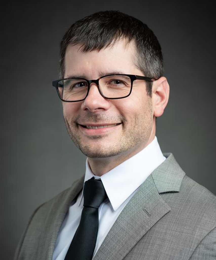 Collin Torok smiles in a grey suite and blue tie.