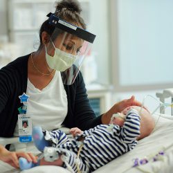 a Children's Minnesota staff member wearing a mask and face shield checks on a baby in the cardiovascular ICU