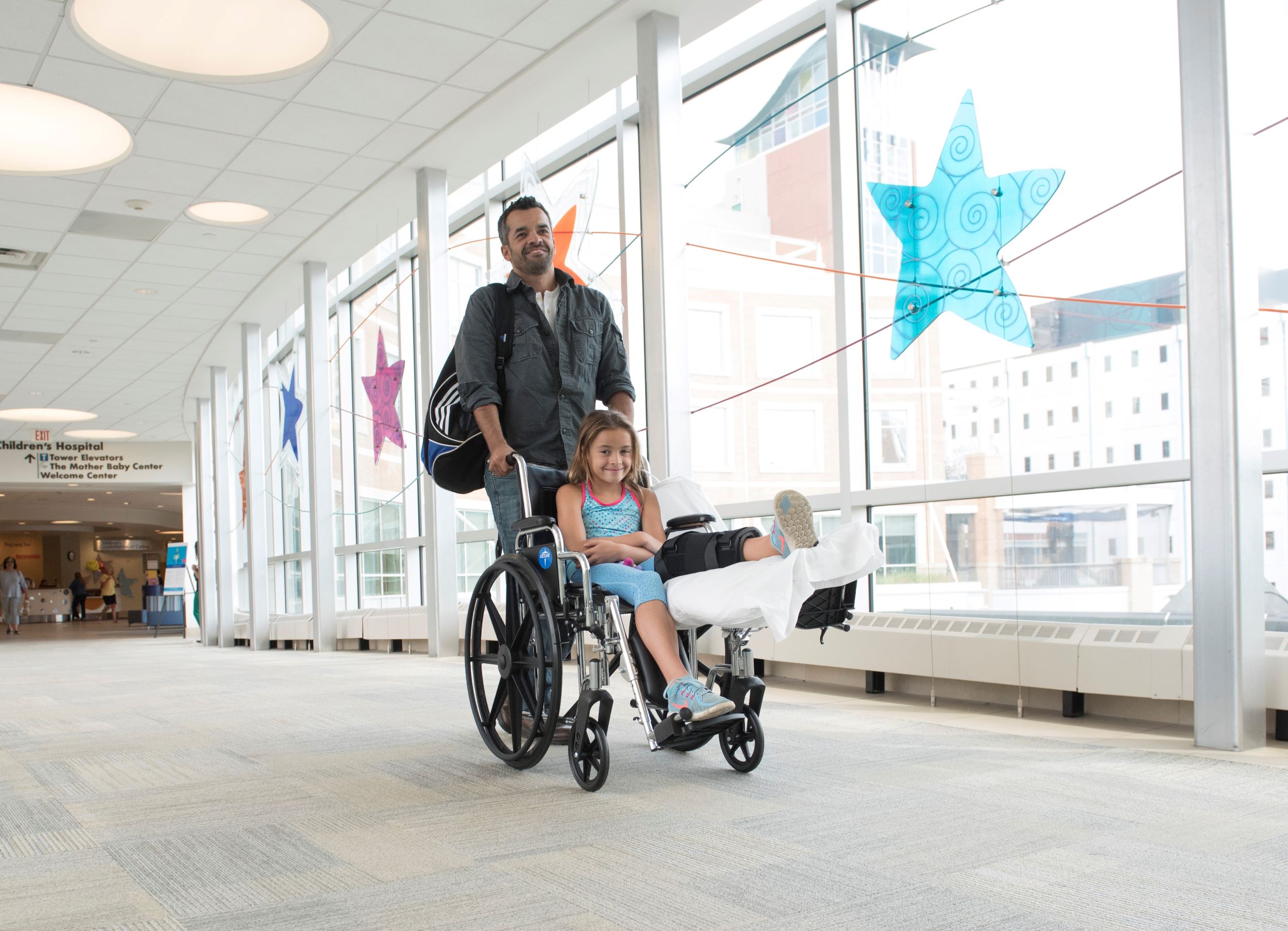 Father pushing daughter in a wheel leaving the hospital after discharge.