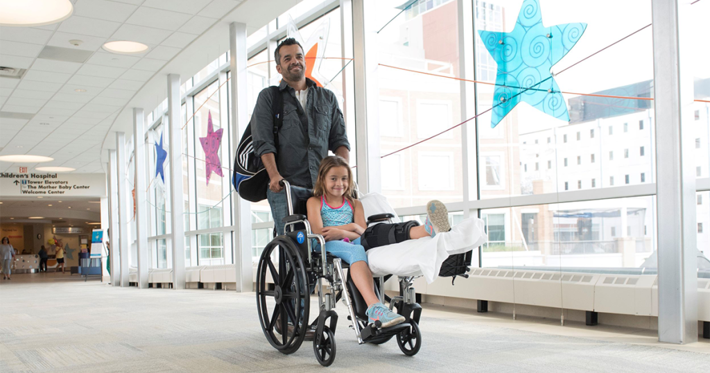 Father pushing daughter in a wheel leaving the hospital after discharge.|