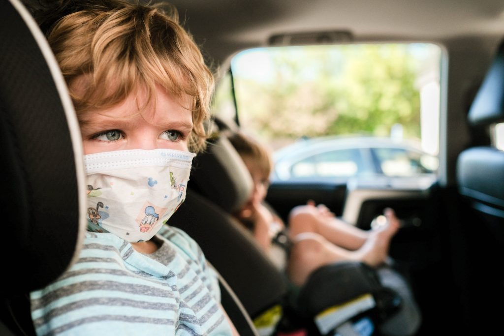 Little boy in a face mask about to get a COVID-19 test int he car.