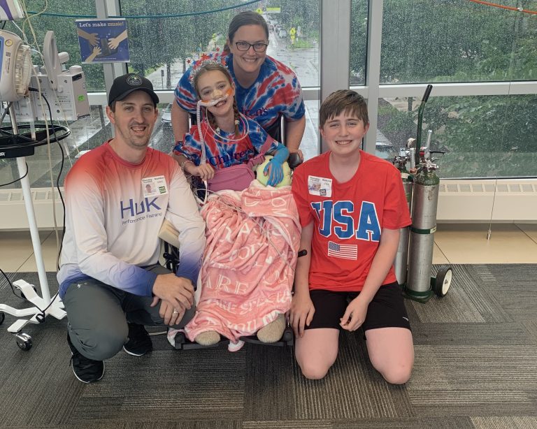 Grace with her parents and brother in a skyway at Children's Minnesota. Grace is hooked up to life supporting machines.