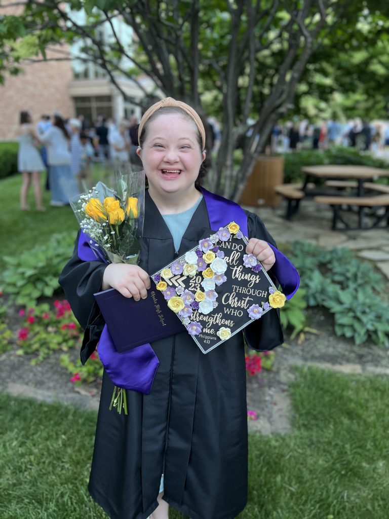 Photo of Elly at her graduation from Chaska High School in June 2023. She's smiling and holding flowers and graduation cap.