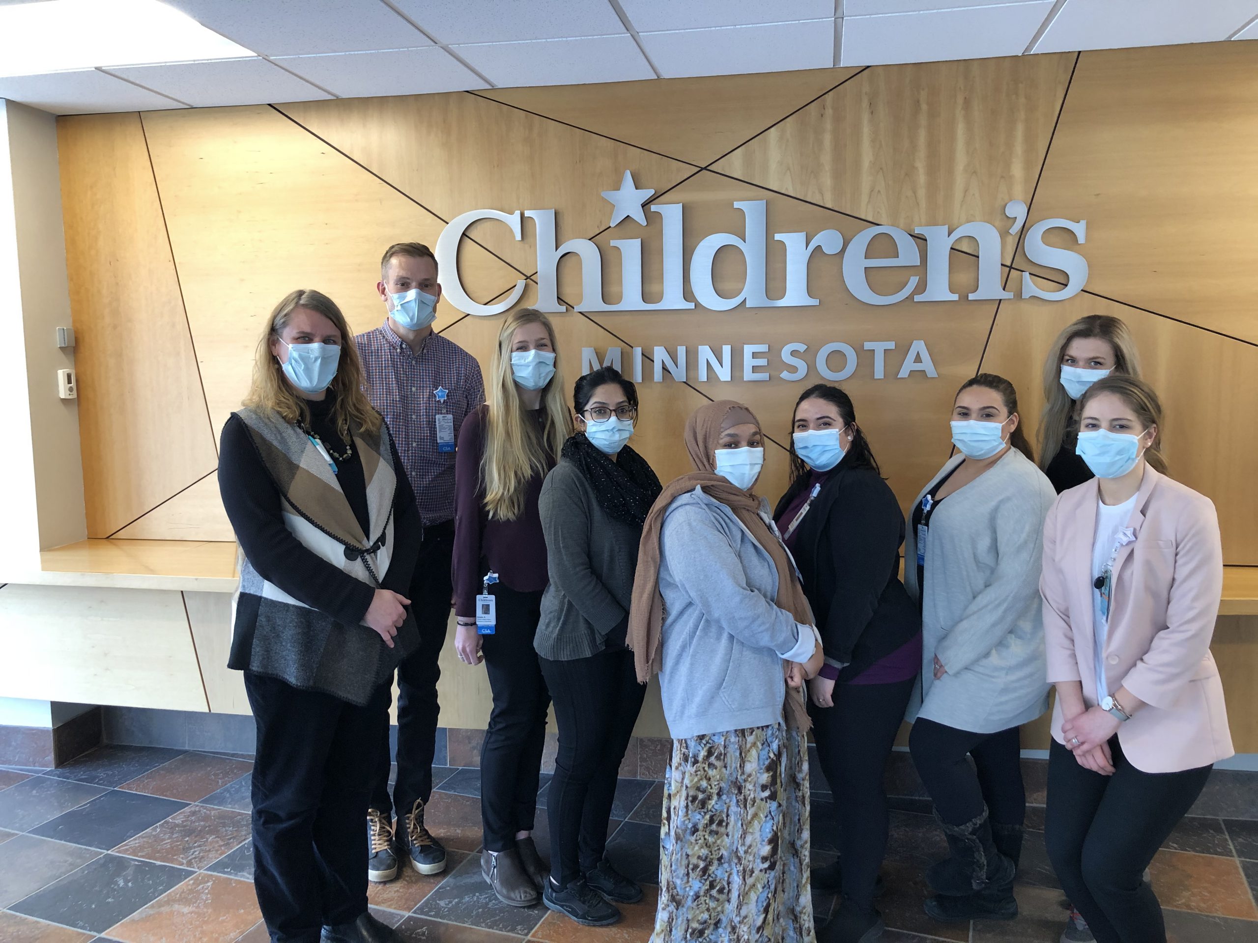 Nine CSAs stand in front of a Children's Minnesota sign. They're all wearing clinical masks.