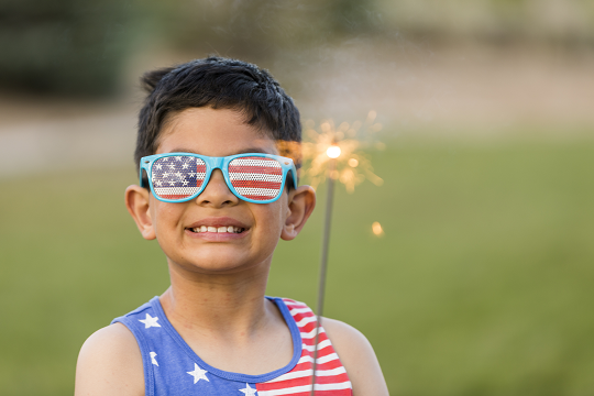 Boy wearing American flag print shirt and glasses uses a sparkler