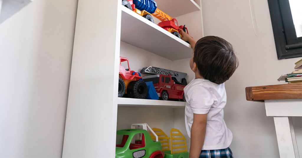 Child reaching for a toy on a tall shelf.