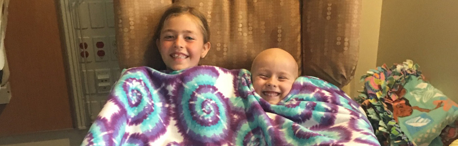 Two girls cuddled in a blanket made by classmates.