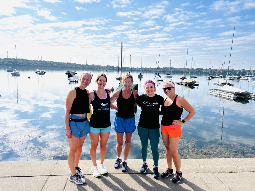 A small group of the cancer and blood disorders staff running in the marathon standing by a lake.