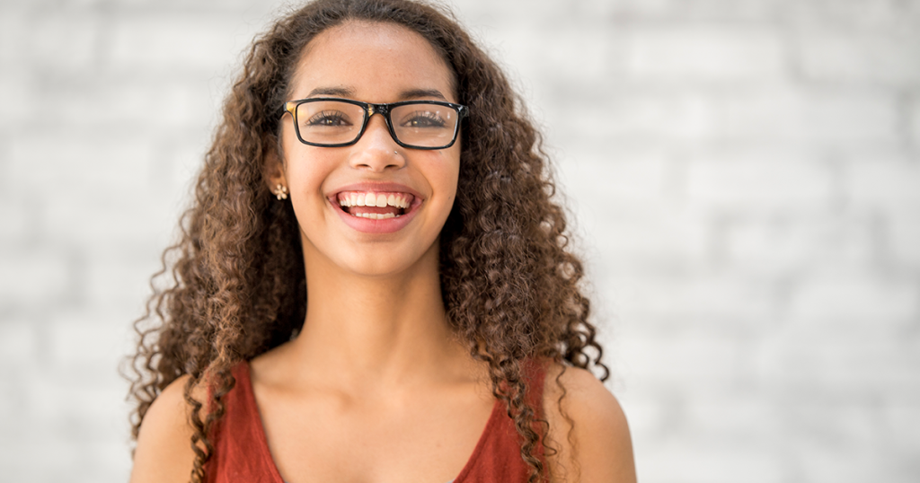 Teenage girl with curly hair and glasses smiling.