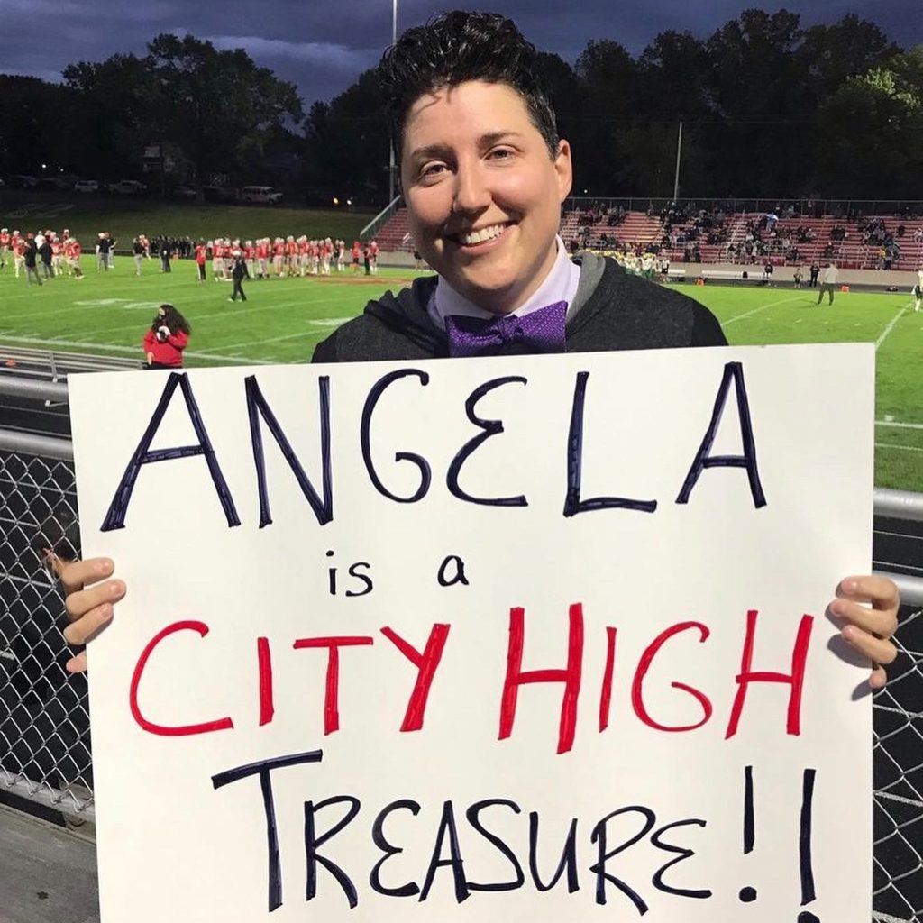 Dr. Kade Goepferd holding a poster that says "Angela is a City High treasure!"