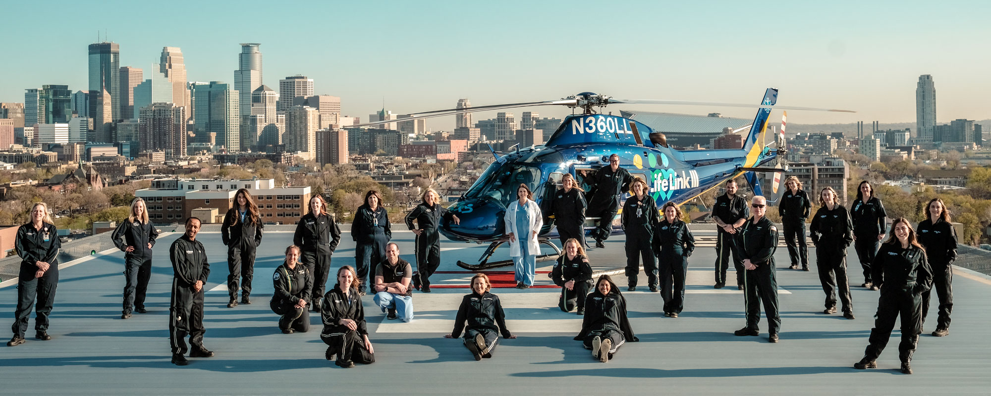 the neonatal transport team of 25 people stand on the roof of the hospital. Behind them is the Life Link helicopter