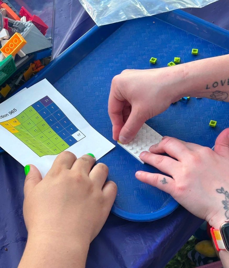 Photo of people's hands pressing LEGOs to make the You Belong LEGO mural.