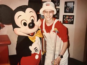 Jennifer Pratt as a child smiling next to Mickey Mouse at Disney World