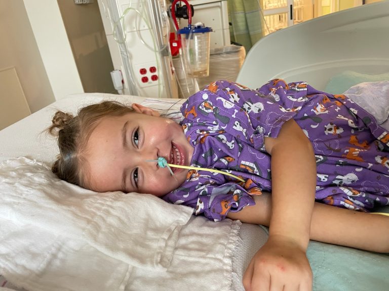 Sydney in a hospital bed smiling