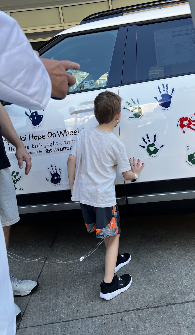 Child putting their painted hand and leaves handprint on a Hyundai SUV.