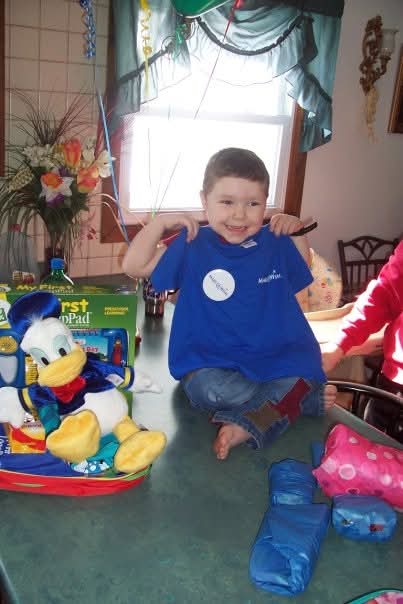 Young Jentai holds up blue shirt and smiles.