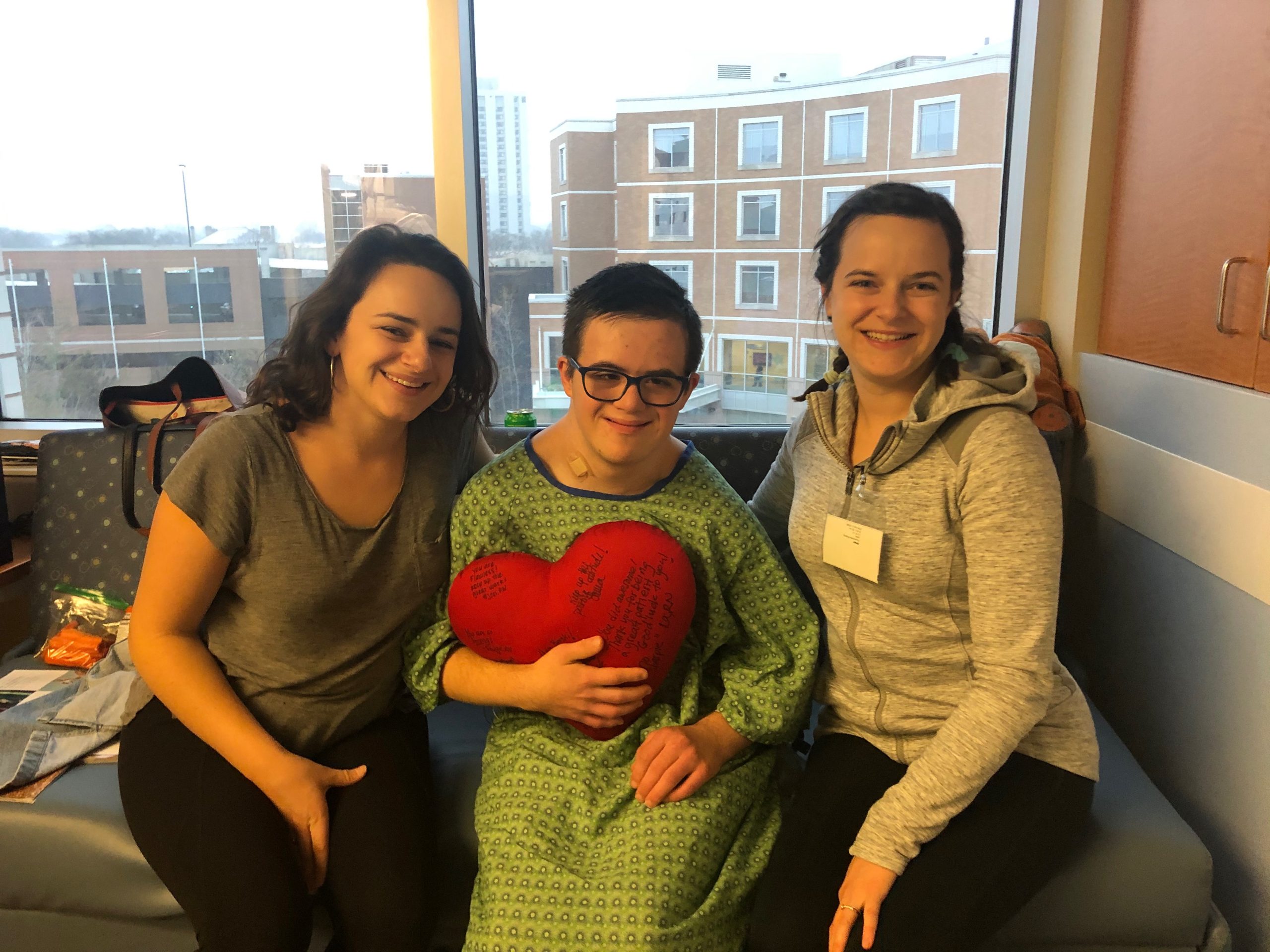 Michael and his sisters at Children's Minnesota sitting on his hospital bed with a heart pillow