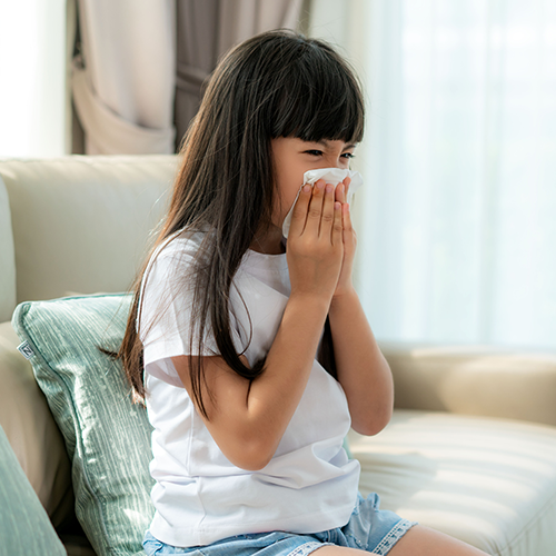 Young child blowing her nose into a Kleenex.