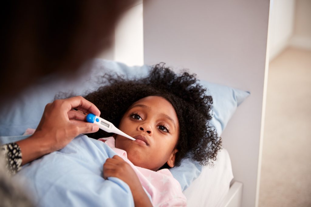 Mother taking daughter's temperature while she is in bed.
