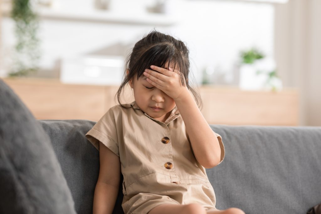 Little girl having a headache on the couch at home.
