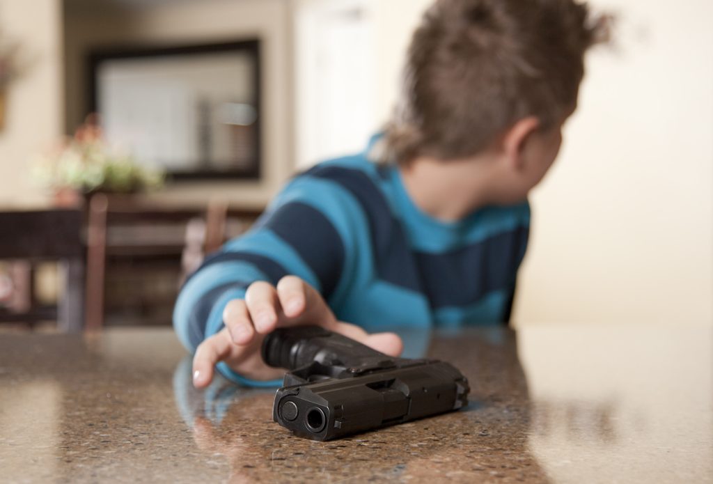 Older boy about 11 years old reaching for a hand gun that has been left unattended on the kitchen counter top and is looking behind him to see if anyone is looking. Gun is the focal point.
