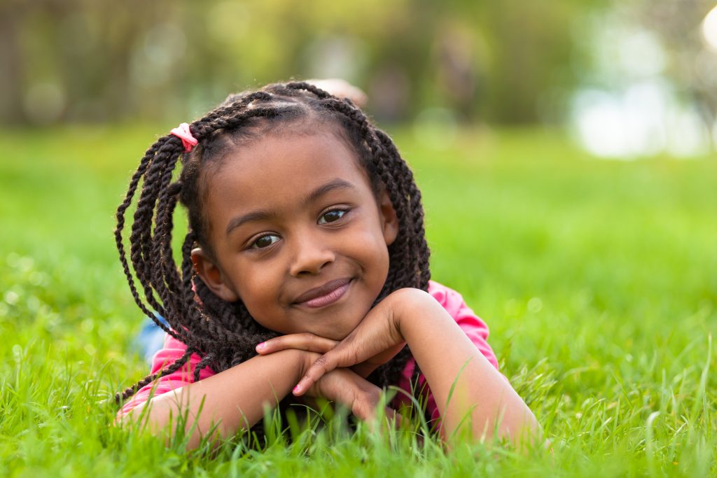 Outdoor portrait of a cute young black girl lying down on the grass and smiling
