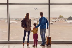 Family of three looking out the airport window at an airplane